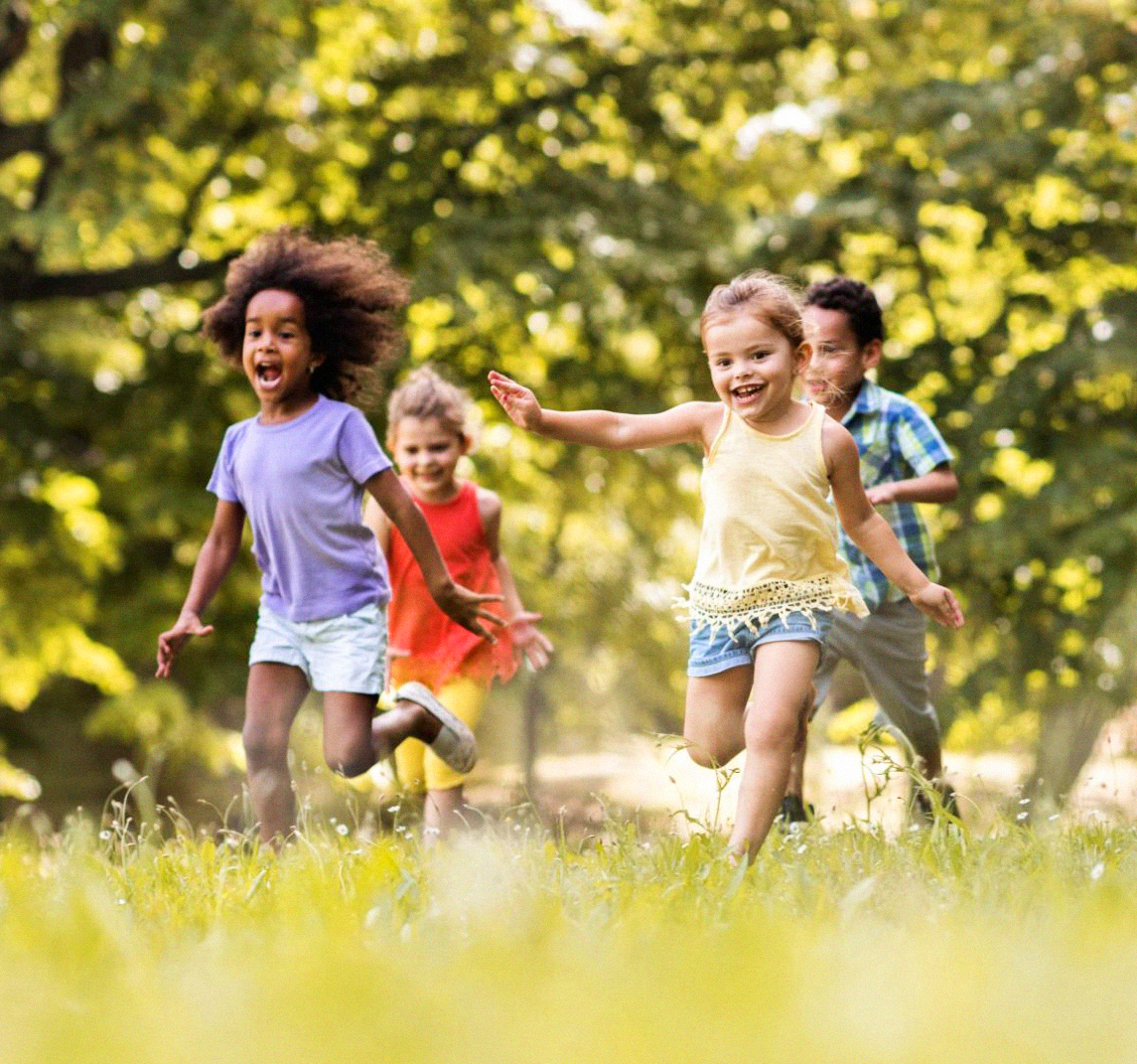 Children of diverse ethnicities running in grass with tree canopies behind them